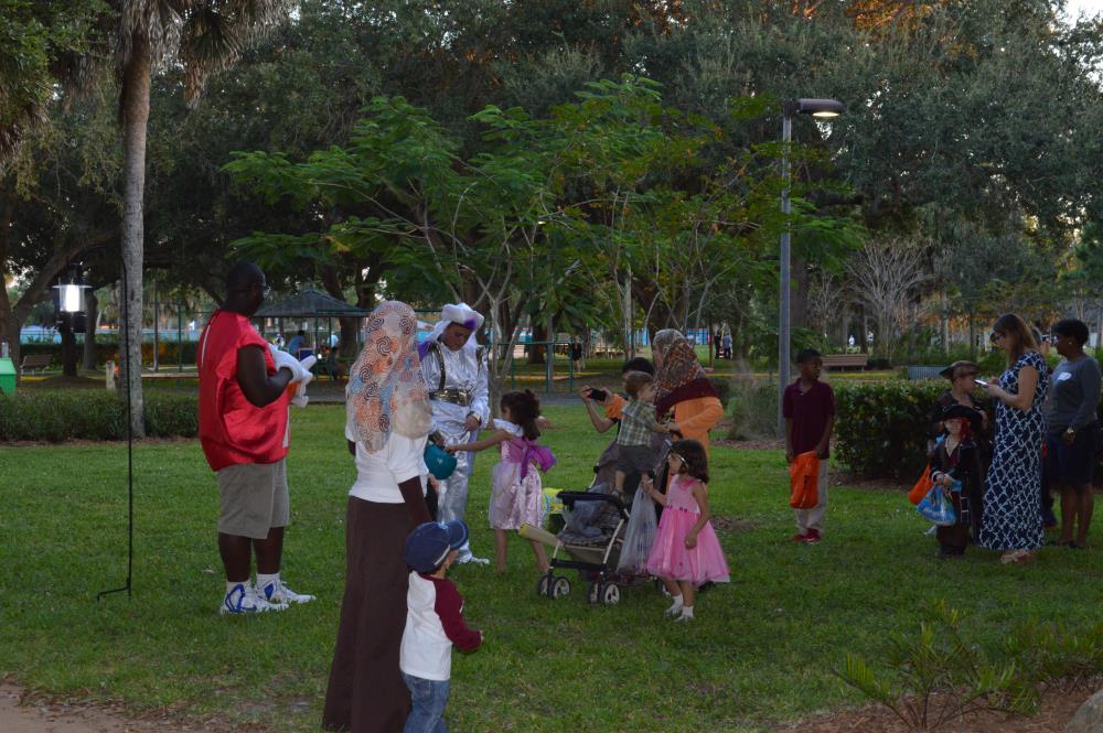 Man dressed as red M&M and man dressed as a sultan hand out candy to children dressed in Halloween costumes